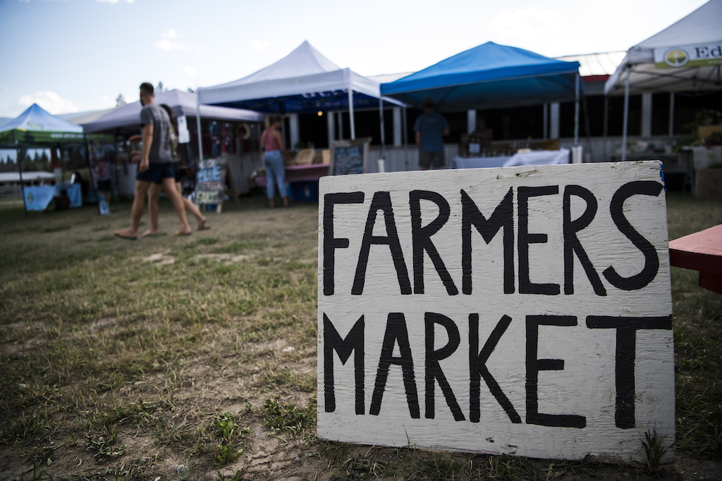 A photo of a sign that reads Farmers Market placed in front of a farmers market